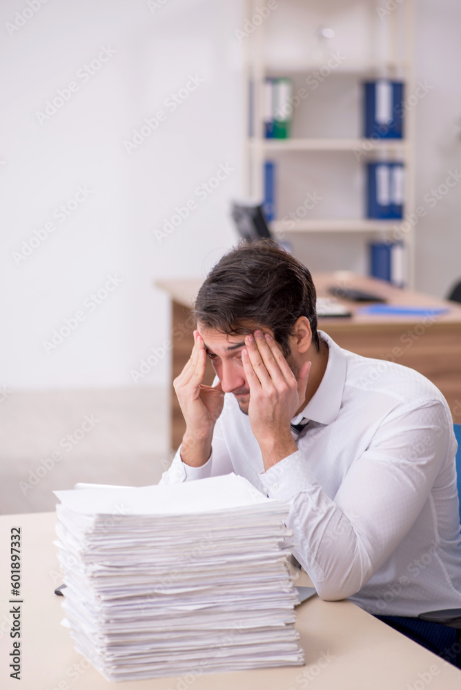 Young male employee unhappy with excessive work in the office Young male employee unhappy with excessive work in the office