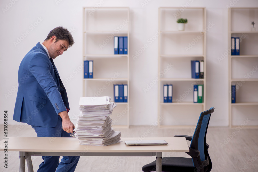 Young male employee unhappy with excessive work in the office Young male employee unhappy with excessive work in the office