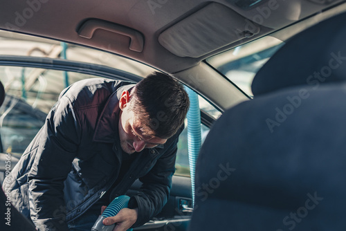 A young man vacuums the interior of a car.