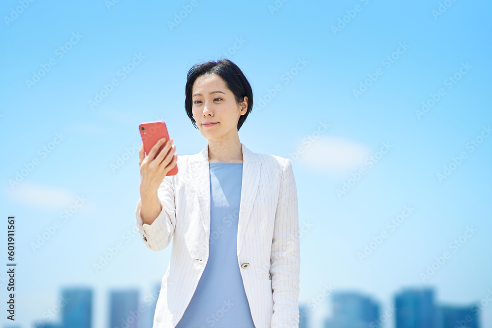 晴天の屋外でスマートフォンを持つビジネスウーマン 晴天の屋外でスマートフォンを持つビジネスウーマン