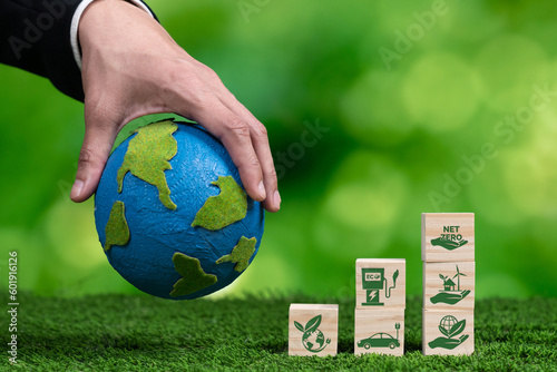 Businessman hand with paper globe and net zero symbol cube for eco awareness. Ethical company reduce CO2 emission, fight climate change and global warming by clean energy for green environment. Alter