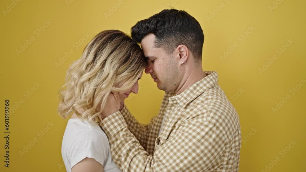 Man and woman couple hugging each other kissing head over isolated yellow background Man and woman couple hugging each other kissing head over isolated yellow background