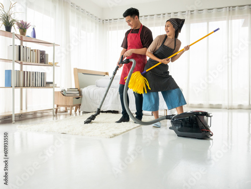 Asian family brother and sister dancing and cleaning a white living room with vacuum cleaner and yellow twist mob fiber on the floor and rug in the weekend at home