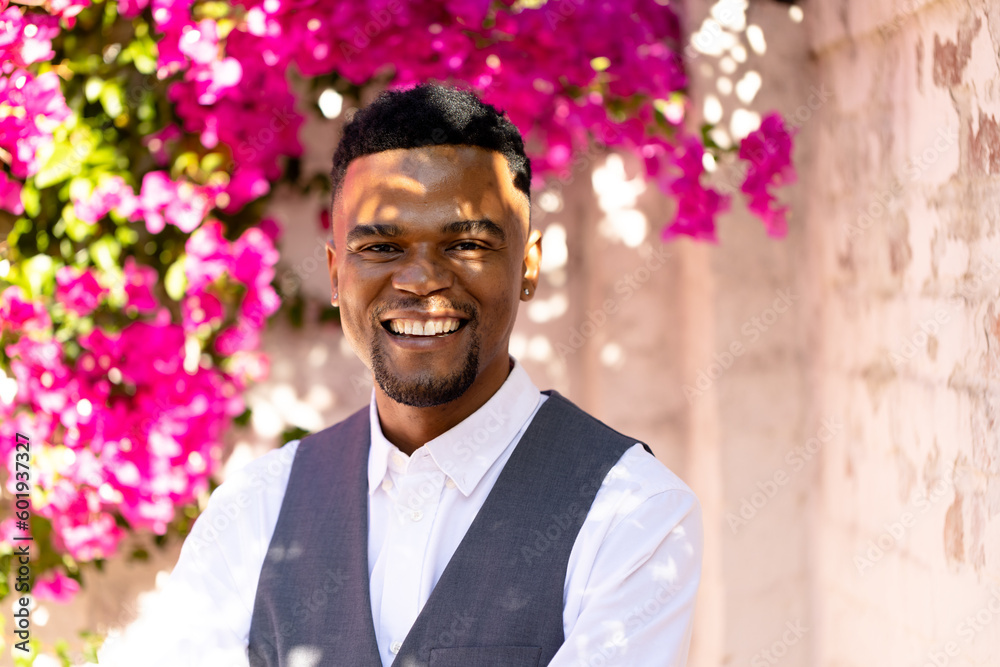 Smiling african american young gay man dressed in suit standing against cheery blossom and wall Smiling african american young gay man dressed in suit standing against cheery blossom and wall