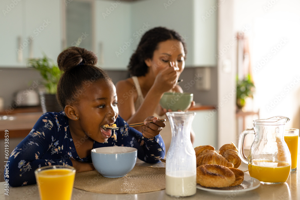 Happy african american mother and daughter sitting at kitchen island eating breakfast together Happy african american mother and daughter sitting at kitchen island eating breakfast together