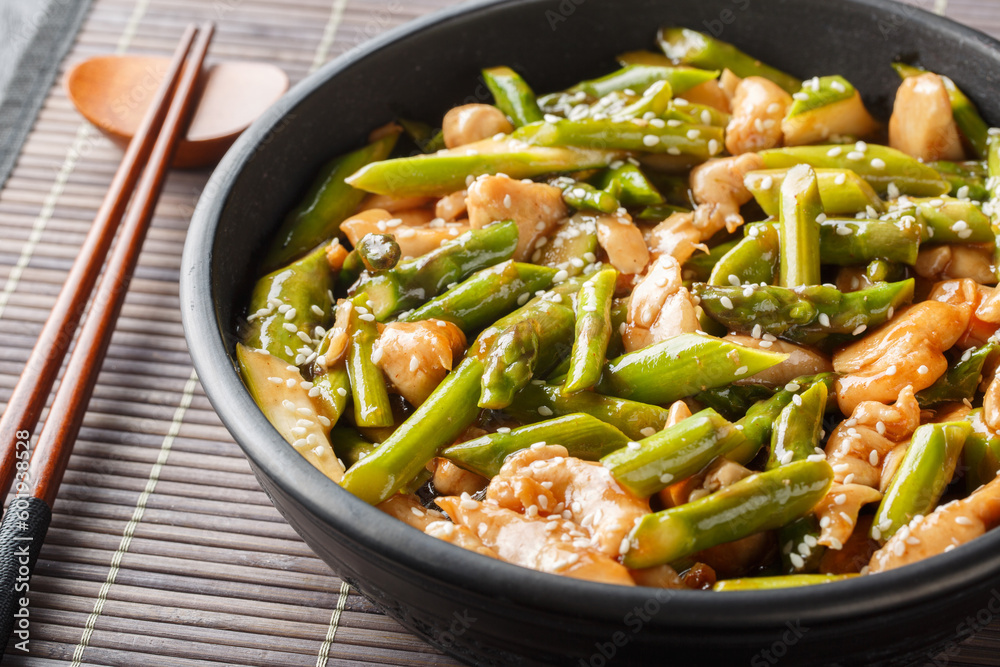 Delicious fried chicken fillet with asparagus and sesame seeds in soy sauce close-up in a bowl on the table. Horizontal Delicious fried chicken fillet with asparagus and sesame seeds in soy sauce close-up in a bowl on the table. Horizontal