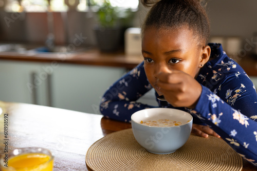 Happy african american girl eating breakfast cereal sitting in kitchen, with copy space photo