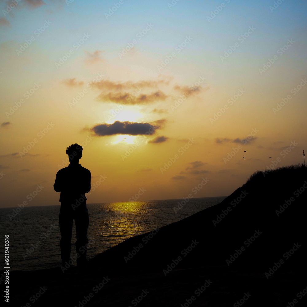 the silhouette image of a sad boy standing near an ocean with sky in the background the silhouette image of a sad boy standing near an ocean with sky in the background