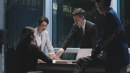 team of four asian corporate executives meeting in office at night discussing business strategy