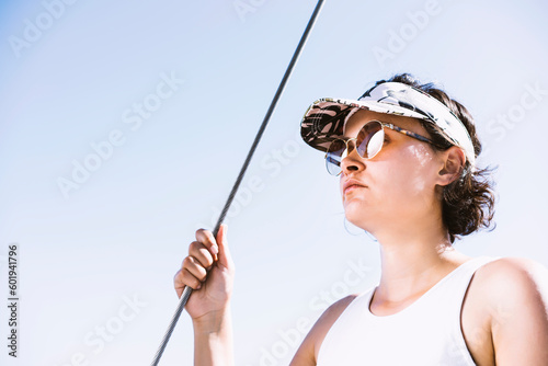 Woman wearing tennis cap and sunglasses on boat deck holding sail rope