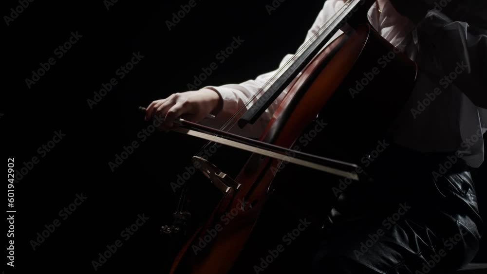 Female musician plays classical music on cello while sitting on chair in studio, dark background, side view. Woman musician plays music at cello