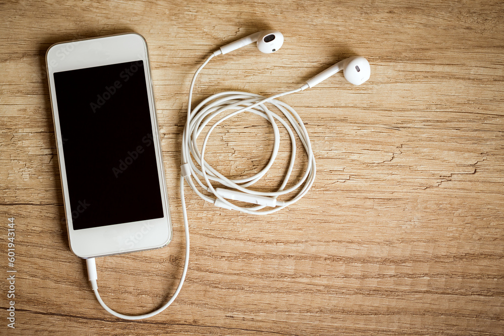 Close-up of smart phone with headphones on a wooden background. (Top view). Listen to music. Close-up of smart phone with headphones on a wooden background. (Top view). Listen to music.