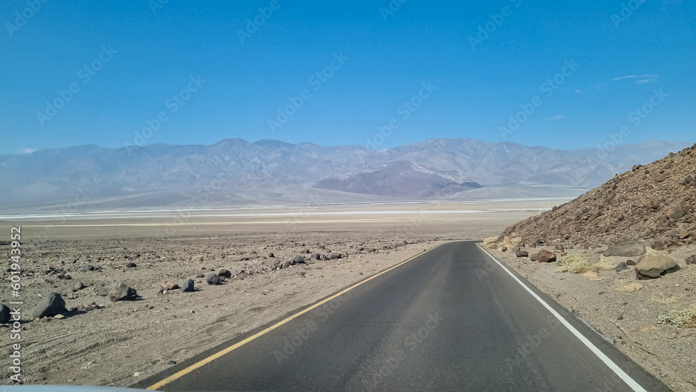 Panoramic view of endless empty road leading to colorful geology of multi hued Artist Palette rock formations in Death Valley National Park near Furnace Creek, California, USA. Black mountains