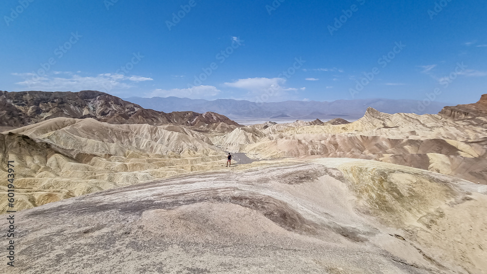 Man with scenic view Badlands of Zabriskie Point, Furnace creek, Death Valley National Park, California, USA. Erosional landscape of multi hued Amargosa Chaos rock formations, Panamint Range in back