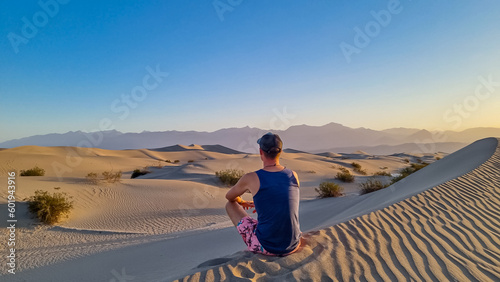 Touristic man enjoying the sunrise with scenic view on Mesquite Flat Sand Dunes, Death Valley National Park, California, USA. Morning walk in Mojave desert with Amargosa Mountain Range in back. photo