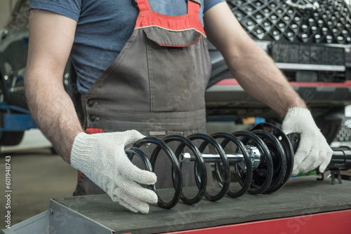 An auto mechanic holds a new shock absorber strut and a spring in his hands. The specialist evaluates the compatibility of the car suspension parts. Car maintenance.
