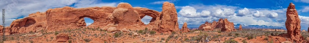 Panoramic view of North Window, South Window, and Turret Arch with beautiful clouds in the sky, small figures of people in the frame emphasize the scale and beauty of this majestic creation, Moab, USA