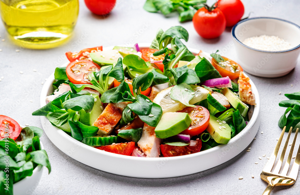 Chicken and vegetables salad with tomatoes, avocado, cucumber, onion, lamb lettuce and sesame seeds on gray table background, top view Chicken and vegetables salad with tomatoes, avocado, cucumber, onion, lamb lettuce and sesame seeds on gray table background, top view