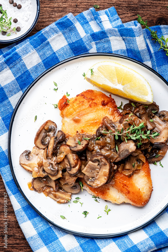 Fried chicken breast with mushrooms and onion sauce with white wine and thyme on plate, old wooden table background, top view