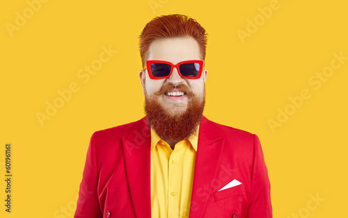 Studio headshot of happy funny fat guy in funky outfit. Head shot of cheerful smiling plump young man with ginger mustache and beard wearing red suit, yellow shirt and cool sunglasses. Fashion concept
