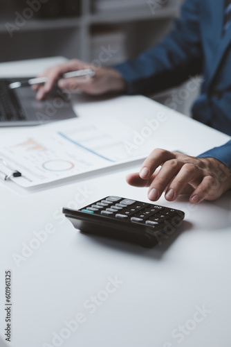 Businessman using a calculator to calculate numbers on a company's financial documents, he is analyzing historical financial data to plan how to grow the company. Financial concept.
