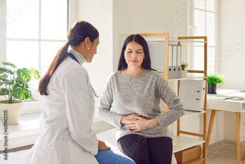 Patient suffering from stomach ache having consultation with female doctor in medical office. Young woman visiting gastroenterologist, gynecologist, therapist, GP in medical clinic photo