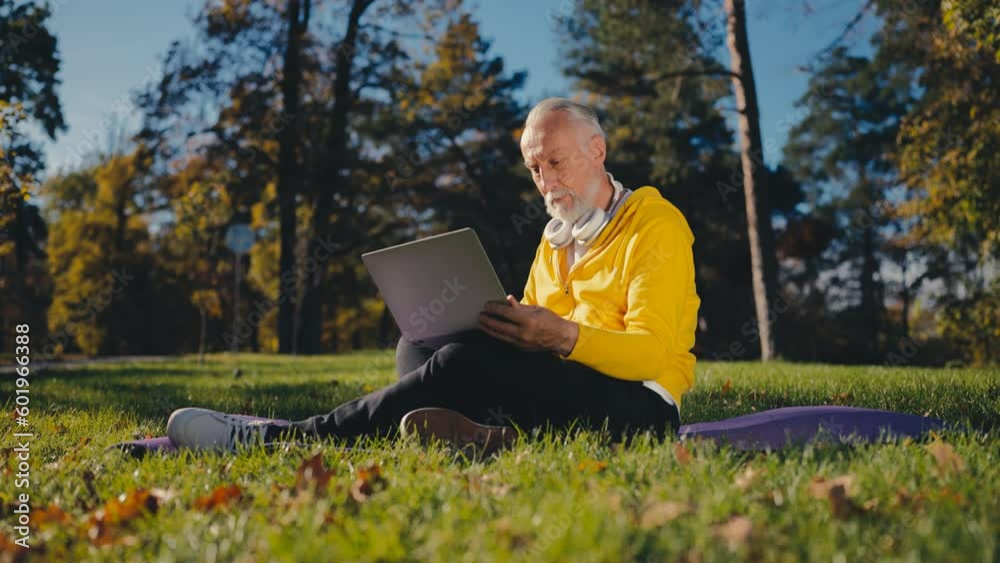 Senior man using laptop while sitting on grass in park, modern technology user Senior man using laptop while sitting on grass in park, modern technology user