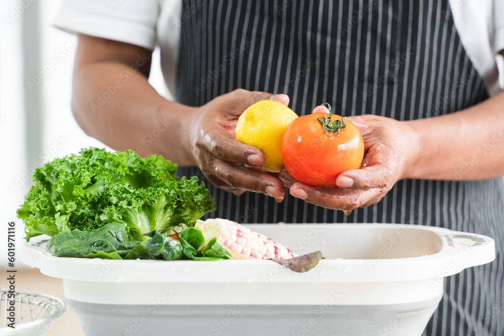 Selective focus on hands of senior man washing tomato and lemon at home. Vegetables, lettuce and corn soak with water in basin. Healthy food and cleaning before cooking concept. Focus on tomato Selective focus on hands of senior man washing tomato and lemon at home. Vegetables, lettuce and corn soak with water in basin. Healthy food and cleaning before cooking concept. Focus on tomato