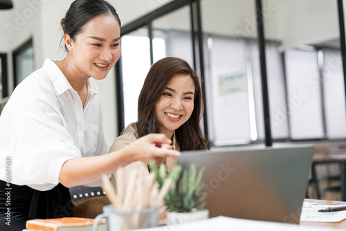 Two young woman working together, smiling and laughing with happiness at office.