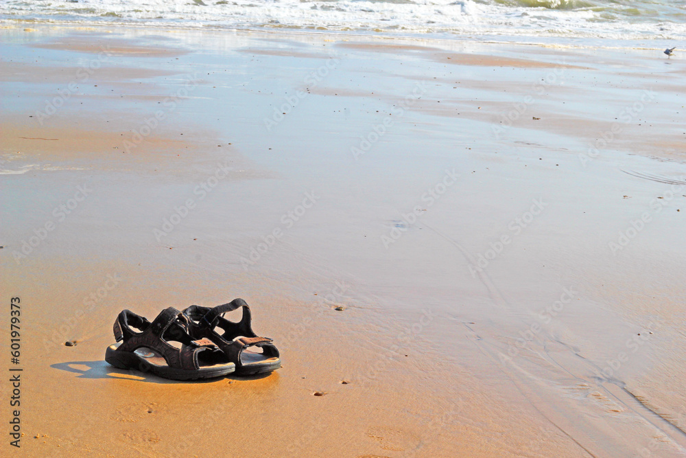 Obraz premium Pair of shoes or sandals left on a beach. Tide gradually coming in on flat sand.