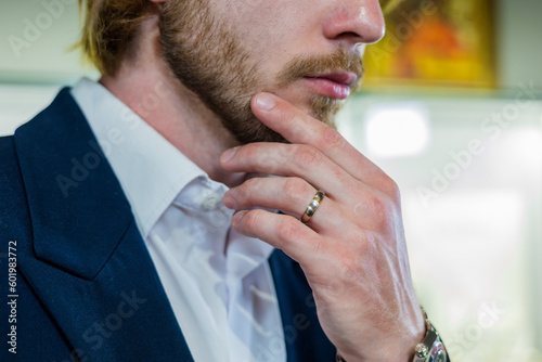 Handsome man in a stylish fashionable suit holds chin at a jewelry store. A male model with a ring on his finger holds face in close-up at a diamond shop.
