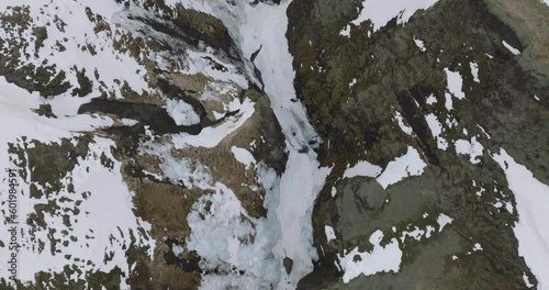 Top Down Drone Shot of Frozen River Under Snow Capped Volcanic Cliffs, Fjadrargljufur Canyon, Iceland photo