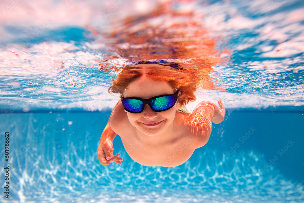 Naklejka premium Kid swimming in pool underwater. Child boy swim underwater in sea. Child playing and diving in swimming pool. Funny kids boy play and swim in sea or pool water. Summer vacation concept.