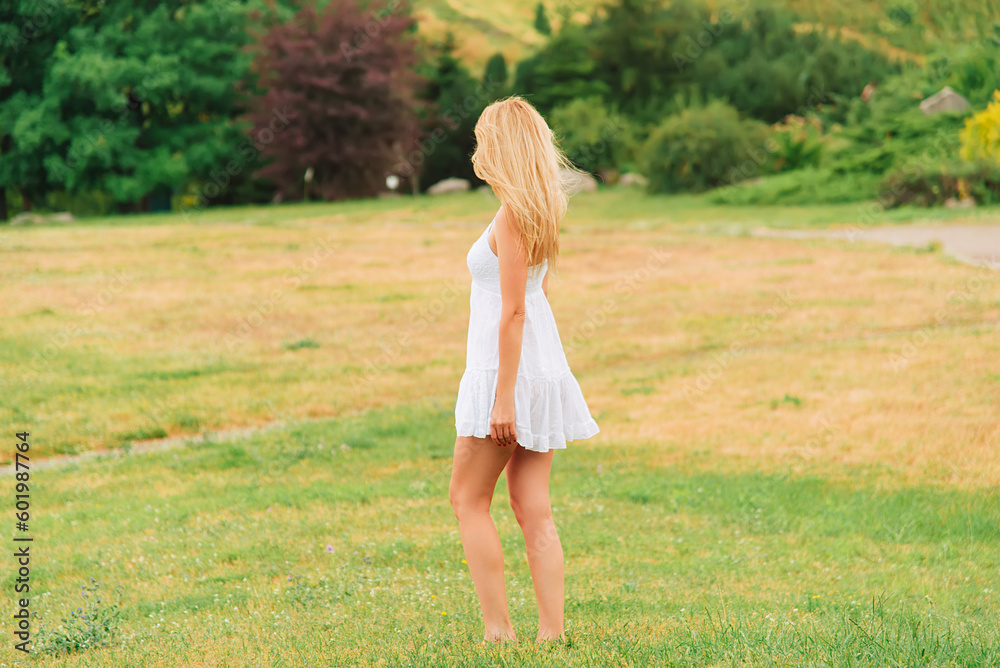 Summer warm day. Woman walks barefoot in the park in a short white dress. Rural landscape. No face, view from the back. Summer warm day. Woman walks barefoot in the park in a short white dress. Rural landscape. No face, view from the back.