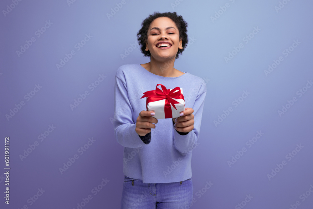 positive young brunette lady with afro curls holds out a gift box positive young brunette lady with afro curls holds out a gift box