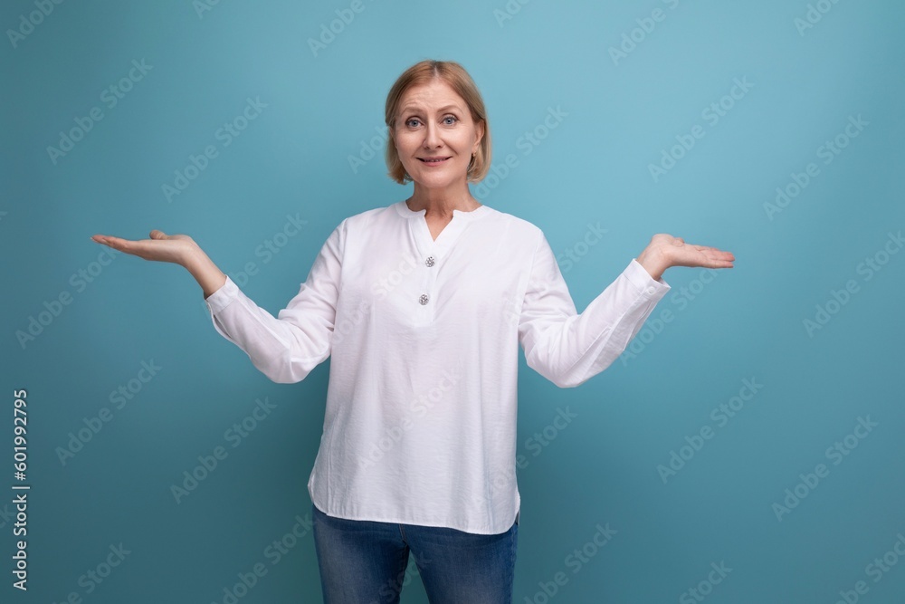 blonde 50s woman in a white blouse in menopause spreads her arms to the sides on a studio background blonde 50s woman in a white blouse in menopause spreads her arms to the sides on a studio background