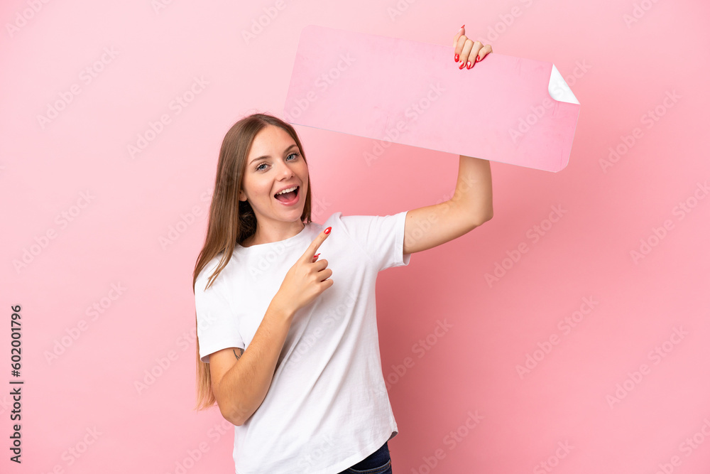 Young Lithuanian woman isolated on pink background holding an empty placard and pointing it Young Lithuanian woman isolated on pink background holding an empty placard and pointing it
