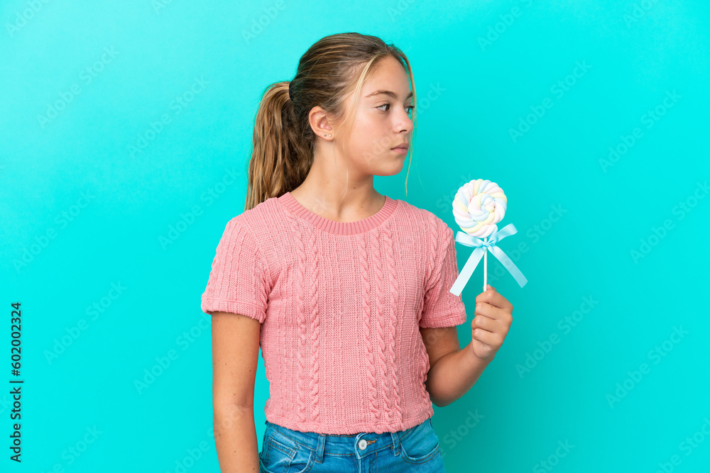 Little Caucasian girl holding a lollipop isolated on blue background looking to the side Little Caucasian girl holding a lollipop isolated on blue background looking to the side