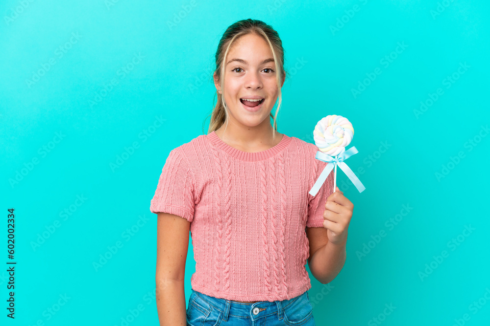 Little Caucasian girl holding a lollipop isolated on blue background with surprise facial expression Little Caucasian girl holding a lollipop isolated on blue background with surprise facial expression