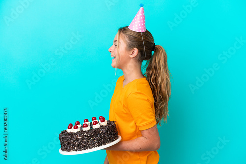 Little caucasian girl holding birthday cake isolated on blue background laughing in lateral position