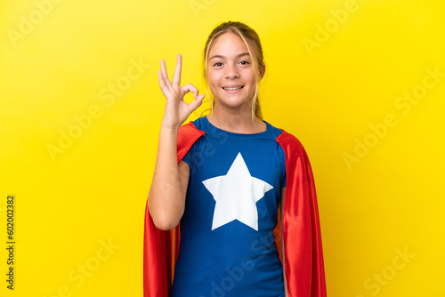 Super Hero little girl isolated on yellow background showing ok sign with fingers