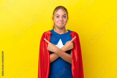 Super Hero little girl isolated on yellow background pointing to the laterals having doubts