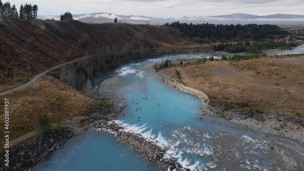 Aerial orbit of kayakers on turquoise glacial water river amidst vast mountainous landscape Aerial orbit of kayakers on turquoise glacial water river amidst vast mountainous landscape