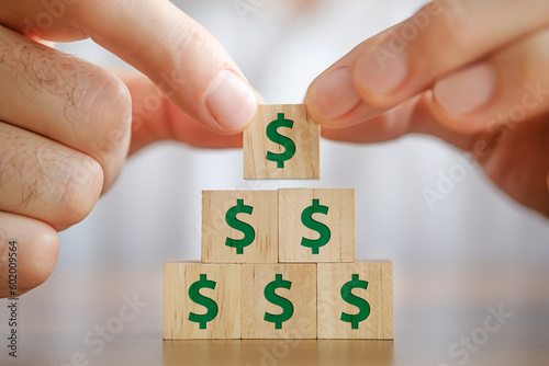 Businessman making a pyramid with wooden blocks with dollar signs on them. Growth concept. 