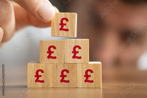 Businessman making a pyramid with wooden blocks with Pound signs on them. Growth concept. 