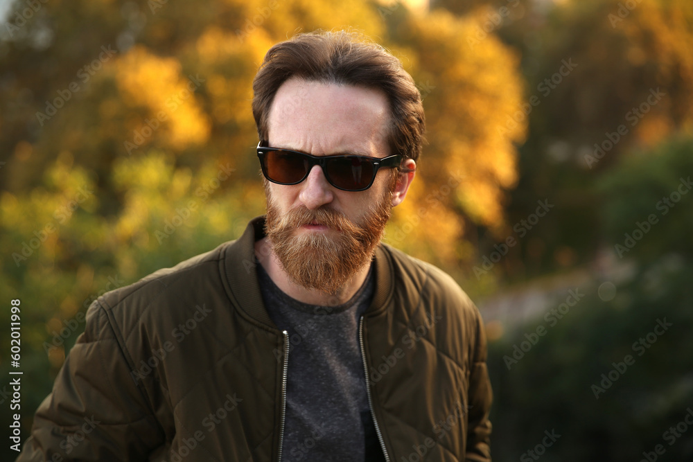 Bearded Caucasian man with sunglasses posing in front of a blurry background with soft natural light Bearded Caucasian man with sunglasses posing in front of a blurry background with soft natural light