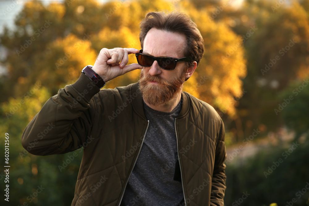 Bearded Caucasian man with sunglasses posing in front of a blurry background with soft natural light Bearded Caucasian man with sunglasses posing in front of a blurry background with soft natural light