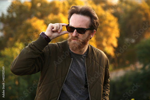 Bearded Caucasian man with sunglasses posing in front of a blurry background with soft natural light © CFK