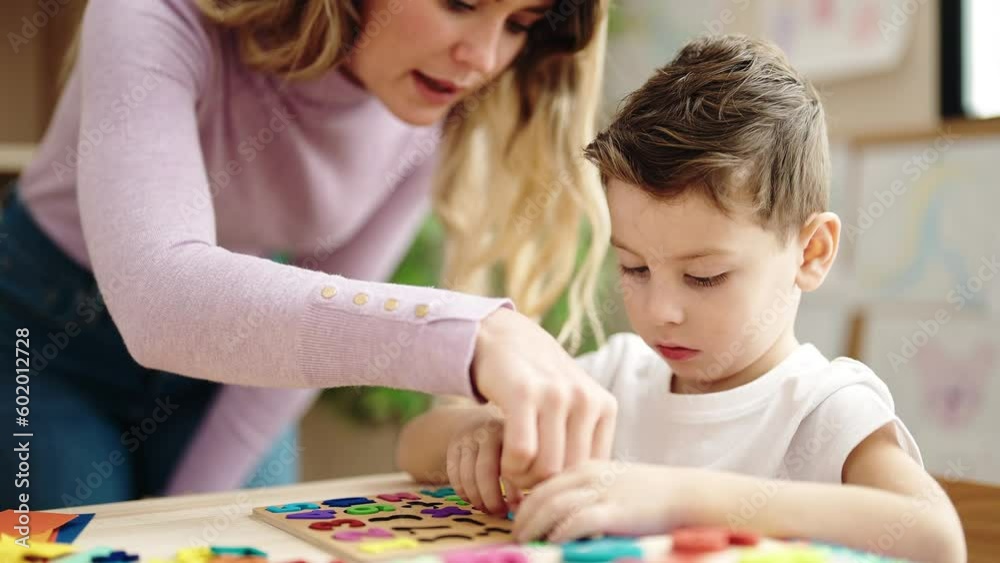 Woman and boy playing with maths puzzle game sitting on table at kindergarten Woman and boy playing with maths puzzle game sitting on table at kindergarten