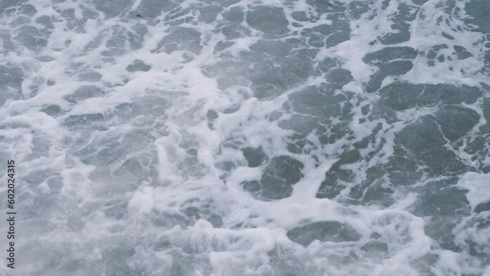 The sea wave breaks on the pebbly shore and rocks and turns into white foam with bubbles. View from above. Nature and environment of Sochi and Tuapse. The sea wave breaks on the pebbly shore and rocks and turns into white foam with bubbles. View from above. Nature and environment of Sochi and Tuapse.